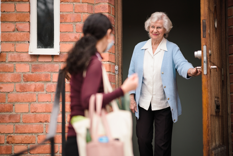 A Home Instead carer arriving at a woman's home offering care support. Woman in opening her front door and smiling