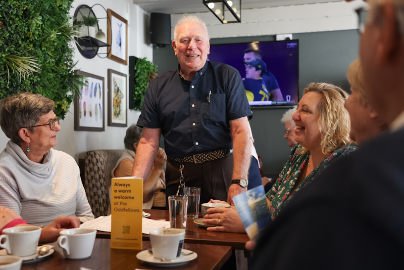 A man stood at a table smiling while others are seated