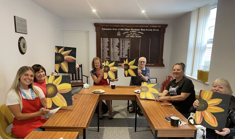 A group of people smiling holding up paintings they've done