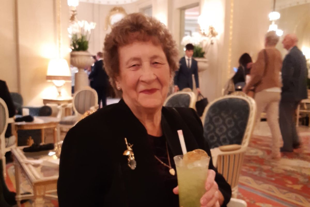 Gwen sits smiling with a drink in her hand