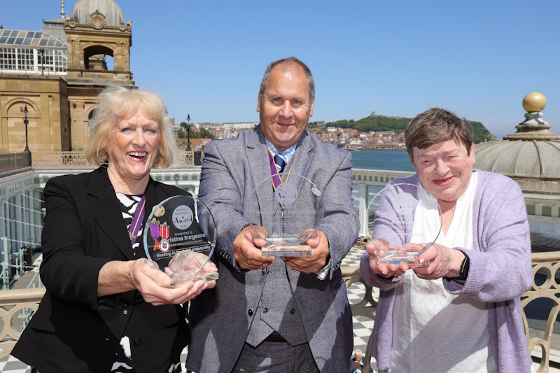 Three people holding glass trophies