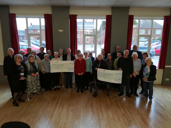 Lots of people stood holding two large cheques